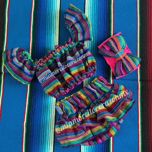 Op de afbeelding: Een kleurrijke gestreepte crop top en rok set met een bijpassend hoofdband. De stof is een geweven katoenmix met een traditioneel Mexicaans ontwerp.