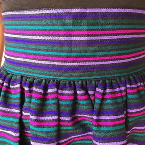 May include: A black skirt with a wide elastic waistband and a gathered skirt. The skirt has horizontal stripes in shades of purple, pink, teal, and blue.