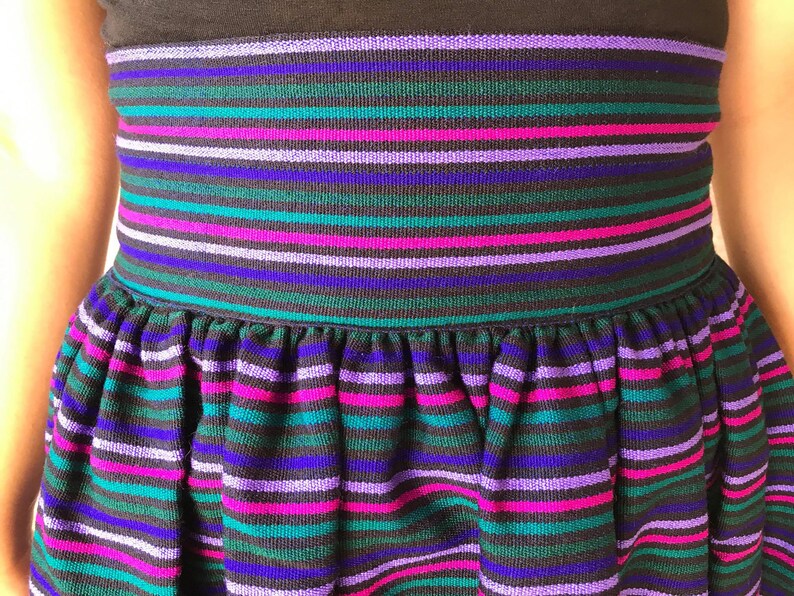 May include: A black skirt with a wide elastic waistband and a gathered skirt. The skirt has horizontal stripes in shades of purple, pink, teal, and blue.