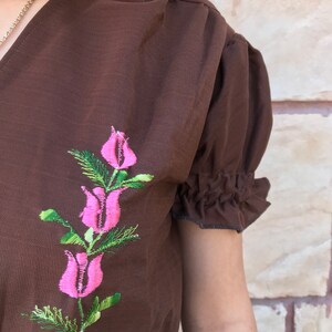 May include: A brown short-sleeved blouse with a pink floral embroidery design.