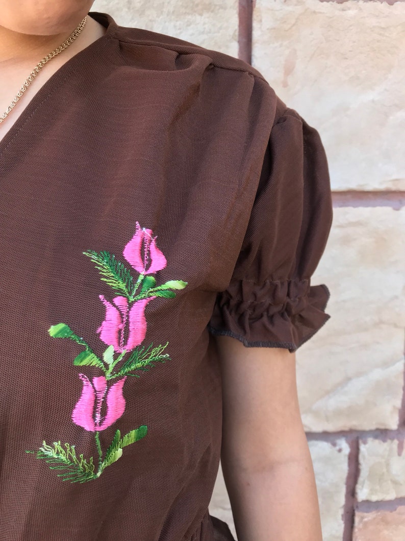 May include: A brown short-sleeved blouse with a pink floral embroidery design.