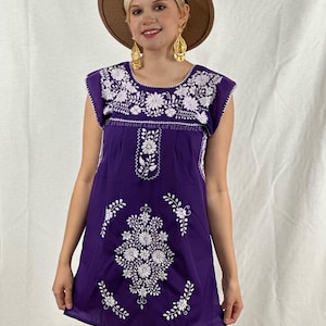 Könnte beinhalten: Ein lilafarbenes besticktes Kleid mit weißen Blumenmustern. Das Kleid hat einen runden Ausschnitt und kurze Ärmel.