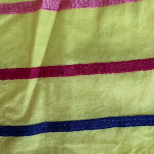 May include: Yellow fabric with three horizontal stripes. The top stripe is pink, the middle stripe is red, and the bottom stripe is dark blue.