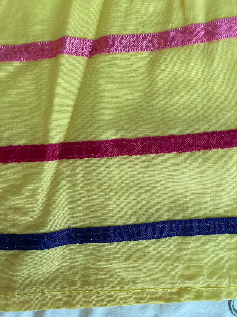 May include: Yellow fabric with three horizontal stripes. The top stripe is pink, the middle stripe is red, and the bottom stripe is dark blue.