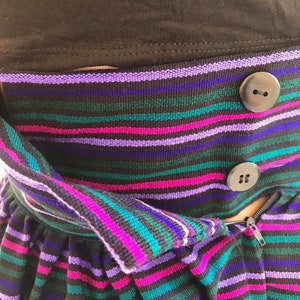May include: A striped skirt with a zipper and buttons. The skirt is made of a soft, stretchy fabric and has a high waist. The colors of the stripes are purple, pink, teal, and black.