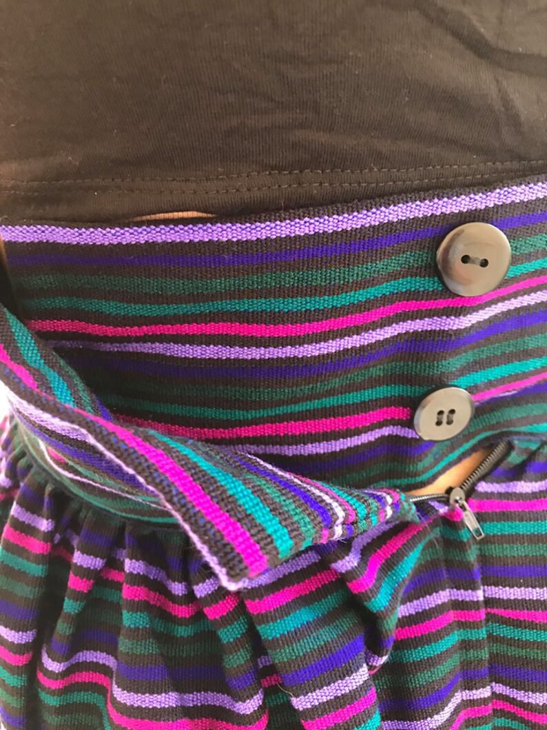 May include: A striped skirt with a zipper and buttons. The skirt is made of a soft, stretchy fabric and has a high waist. The colors of the stripes are purple, pink, teal, and black.