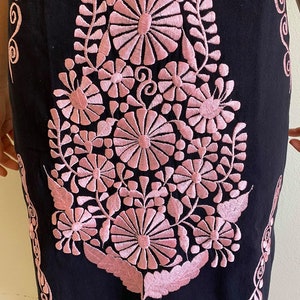 May include: Black linen dress with pink embroidered floral design. The embroidery features a large central flower with smaller flowers and leaves surrounding it.