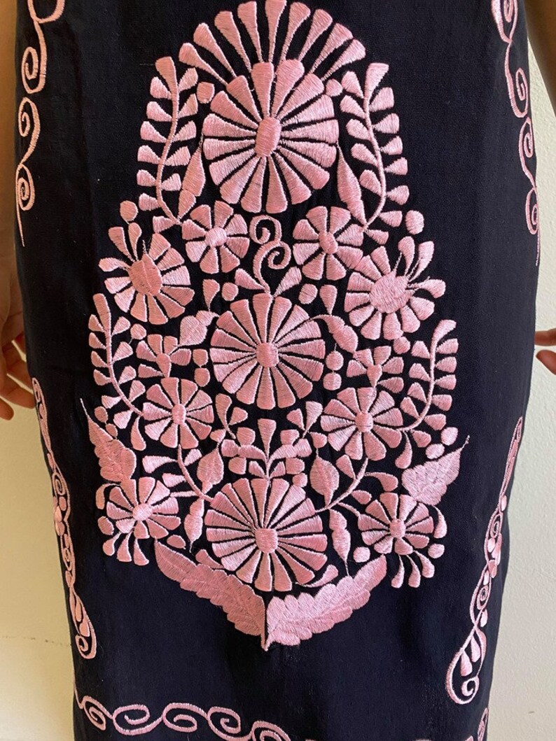 May include: Black linen dress with pink embroidered floral design. The embroidery features a large central flower with smaller flowers and leaves surrounding it.