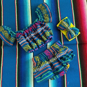 May include: A blue and yellow patterned baby outfit with a matching headband. The outfit includes a ruffled top and shorts. The headband is a yellow bow with a blue and yellow pattern.