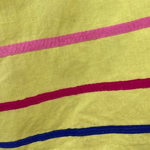 May include: Yellow fabric skirt with pink, red, and blue trim. The skirt has a simple design and is made of a lightweight material.