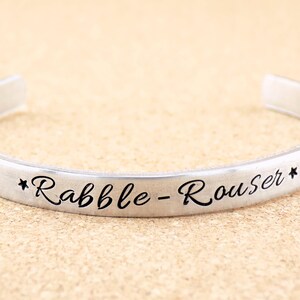 May include: A silver bangle bracelet with the words "*Rabble-Rouser*" engraved on it.