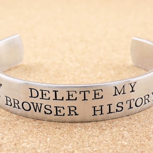 May include: A silver bracelet with the text "DELETE MY BROWSER HISTORY" engraved on it. The bracelet has a medical symbol on each end.