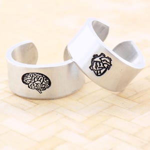 May include: Two silver rings with engraved anatomical designs. One ring features a brain and the other a heart.