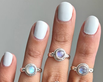 May include: A collection of silver rings with moonstone gemstones. The rings feature various designs, including round and teardrop shapes, with intricate detailing around the stones. The moonstones have a milky, iridescent appearance.