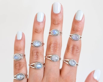 May include: A hand displaying several silver rings with oval, light blue gemstones. The rings have a split band design. The background is plain white, highlighting the jewelry.