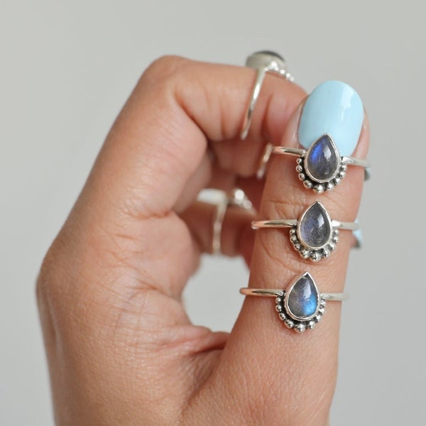 May include: Three silver rings with teardrop-shaped, iridescent gemstones are displayed. Each ring features a beaded design around the gemstone. The rings are on a finger with a light blue nail polish.
