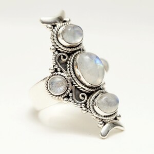 Peut inclure: Une bague de d&eacute;claration argent&eacute;e orn&eacute;e de plusieurs cabochons de pierre de lune ovales et ronds. La bague pr&eacute;sente un design orn&eacute; et d&eacute;taill&eacute; avec des accents en forme de corde et perl&eacute;s. Les pierres de lune ont une qualit&eacute; laiteuse et iris&eacute;e.
