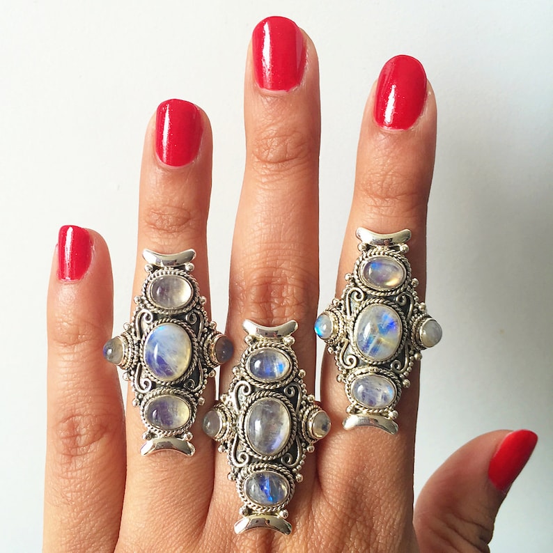 Peut inclure: Trois bagues en argent orn&eacute;es de pierres de lune ovales et rondes. Les bagues pr&eacute;sentent un motif en filigrane et sont pr&eacute;sent&eacute;es sur une main avec du vernis &agrave; ongles rouge.