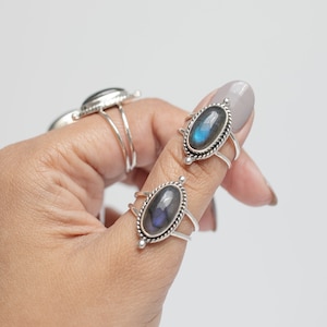 May include: Silver rings with oval-shaped, iridescent labradorite stones. The rings have a twisted rope design around the stone and a double-banded shank. One ring is in focus, with two others visible in the background.