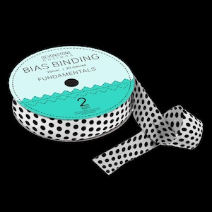 Könnte beinhalten: Eine Spule mit Schrägband mit weißen Grund und schwarzen Punkten. Auf dem Etikett steht "Devonstone Notions Bias Binding 25mm | 20 metres Fundamentals". Das Band ist teilweise abgerollt und zeigt das Punktmuster.