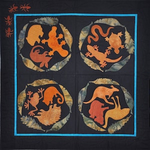 Pode incluir: Um edredom preto com quatro desenhos circulares com silhuetas de animais laranja, incluindo um lagarto e uma cobra, emoldurados por um padrão de folhas. O edredom tem uma borda azul e aplicações de insetos laranja.