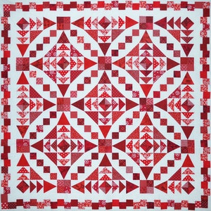May include: A red and white quilt with a geometric pattern. The quilt is made up of squares and triangles, and it has a white background with red accents.