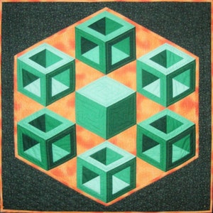 以下が含まれることがあります： 幾何学模様のキルト。中央に緑色の立方体があり、オレンジ色の六角形の背景に6つの開いた緑色の立方体が配置されています。キルトは、小さな花柄のダークグリーンボーダーが付いています。