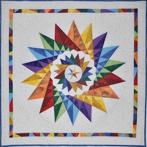 May include: A colorful quilt with a starburst design in shades of red, orange, yellow, green, blue, and purple. The quilt is framed with a multi-colored border.