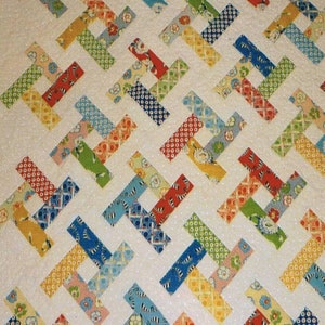 May include: A colorful quilt with a repeating pattern of interlocking rectangles. The rectangles are made of various patterned fabrics in shades of red, blue, green, yellow, and orange, set against a white background with small white dots. The quilt is a patchwork design.