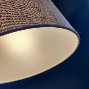 May include: A white fabric lampshade with a textured surface. The lampshade is lit from within, casting a soft, warm glow.