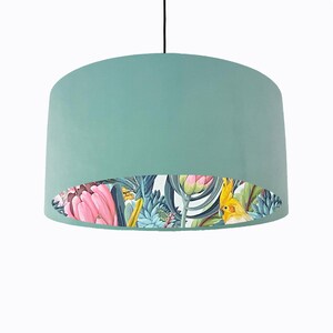 May include: A teal drum lampshade with a floral and bird print lining. The print features pink flowers, green leaves, and a yellow bird.