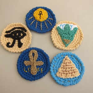 May include: Five crocheted circles featuring various Egyptian symbols. The symbols include the Eye of Horus, Ankh, sun, lotus flower, and pyramid. The circles are beige, blue, and green.