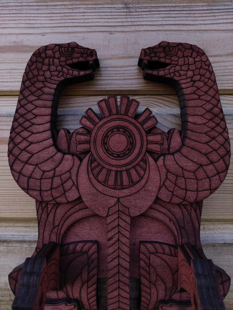 Pu&ograve; includere: Un decoro da parete in legno con una finitura rosso scuro. Il decoro presenta due teste di serpente stilizzate che si fronteggiano, con un disegno circolare al centro. Le teste di serpente hanno una superficie testurizzata, che ricorda le squame.