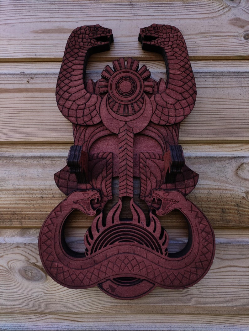 Pu&ograve; includere: Un appendiabiti da parete in legno con un design di due serpenti intrecciati attorno a un simbolo circolare. I serpenti sono scolpiti con un motivo dettagliato e intricato e sono dipinti di un colore rosso intenso.