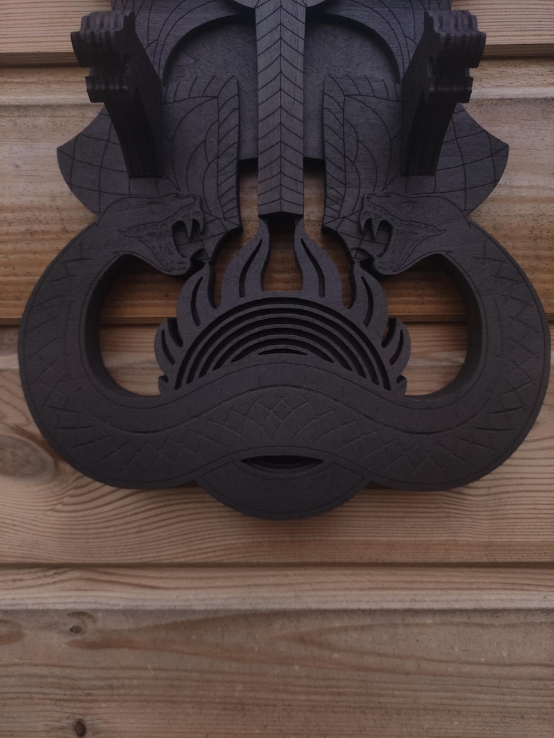 Pu&ograve; includere: Decorazione da parete in legno nero con un design di due serpenti intrecciati attorno a una forma circolare con un design a forma di fiamma al centro.