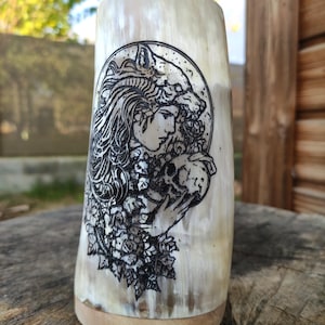 Könnte beinhalten: Ein weißer Trinkhornbecher mit einem schwarz-weißen Design einer Frau mit einem Wolfskopf und Blumen.