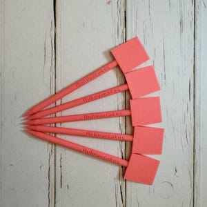 Peut inclure: Cinq outils de décoration de gâteaux en plastique rose avec une pointe carrée et un manche sur lequel est inscrit "Believecakes" en lettres blanches.