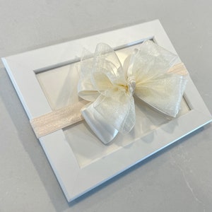 May include: A white headband with a large, white, sparkly bow. The bow is made of tulle and satin.