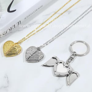 May include: Three silver necklaces with heart-shaped pendants featuring angel wings. The pendants open to reveal a small space inside. One necklace is gold. The third necklace is a keychain.