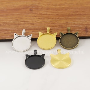 Könnte beinhalten: Fünf katzenförmige Anhänger-Tabletts in verschiedenen Metalloberflächen: Silber, Gold, Bronze, Schwarz und Gold mit gebürsteter Oberfläche. Die Tabletts sind rund und haben einen erhöhten Rand. Sie sind perfekt, um Schmuck eine persönliche Note zu verleihen.