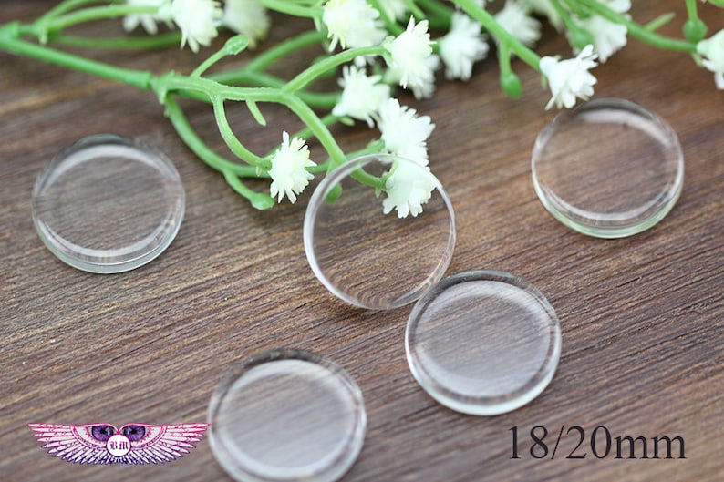 May include: Five clear glass circles, each measuring 18/20 mm in diameter, are arranged on a wooden surface. The circles are slightly raised from the surface and have a smooth, polished finish.