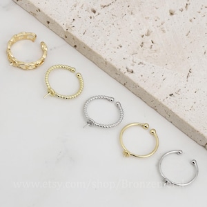 May include: Five different styles of gold and silver ear cuffs. The ear cuffs are made of metal and have a variety of designs, including a twisted rope design, a chain design, and a simple hoop design.