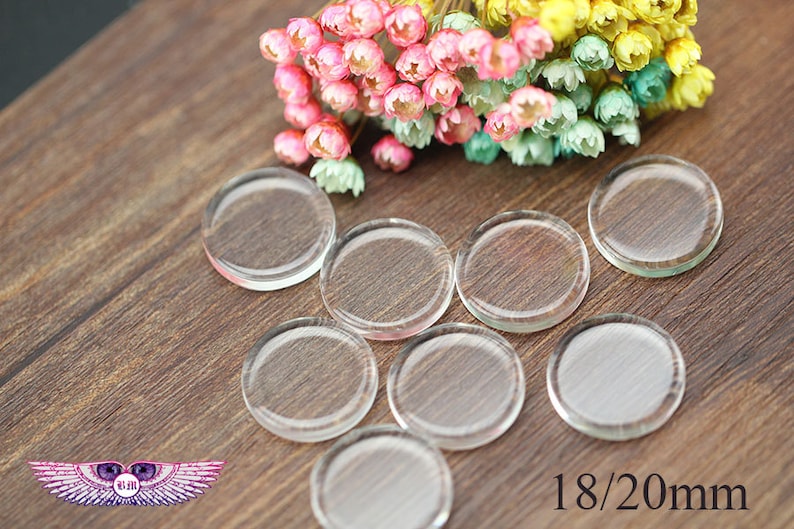 May include: Eight clear glass circles, each measuring 18/20 mm in diameter, are arranged on a wooden surface. The circles are smooth and translucent, with a slight sheen.