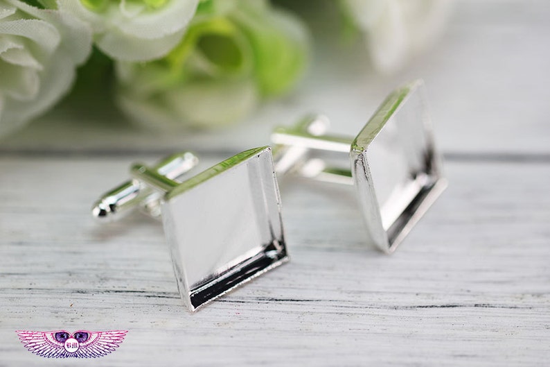 May include: Two silver cufflinks with square glass inserts. The cufflinks are on a white surface.