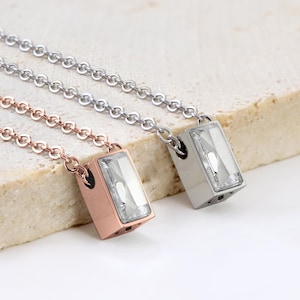 May include: Two necklaces with rectangular, clear crystal pendants. One necklace is rose gold, the other is silver. Both have delicate chain links. The pendants are set in a metal casing.
