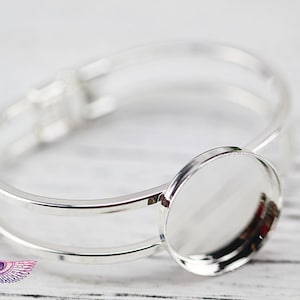 Puede incluir: Pulsera de plata con un cabujón redondo de vidrio en el centro. La pulsera es de doble capa y tiene un diseño simple.