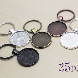 Op de afbeelding: Een verzameling ronde sleutelhangers in diverse metallic afwerkingen, waaronder zilver, brons en zwart. Elke sleutelhanger heeft een ronde basis met een diameter van 25 mm, perfect voor eigen ontwerpen.