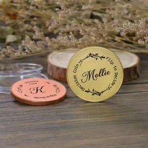 May include: Two decision coins are displayed. One is gold with the name "Mollie" and the words "Decision Coin" and "Flip to Decide." The other is copper with the letter "K" and the same phrases. Both coins have a floral design.