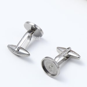 May include: A pair of silver cufflinks with a round, smooth surface. The cufflinks have a simple, classic design.
