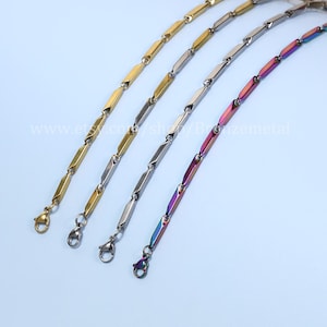 Può includere: Quattro collane a catena diverse con un design a maglie quadrate. Le catene sono dorate, argentate e di un colore arcobaleno iridescente. Le catene hanno tutte la stessa lunghezza e sono dotate di un moschettone.